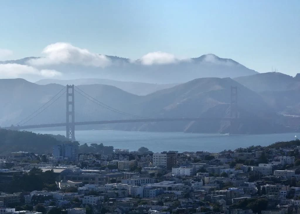 The Golden Gate Bridge and San Francisco skyline seen through haze from a hillside overlook
