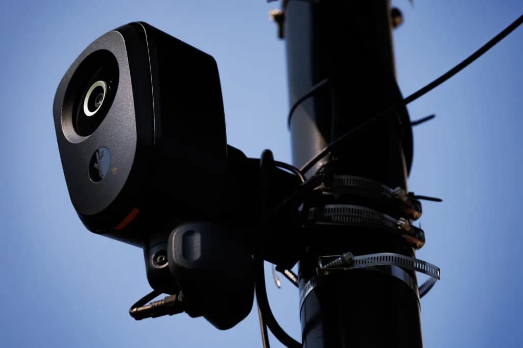 A Flock Safety license plate camera mounted on a utility pole against a blue sky