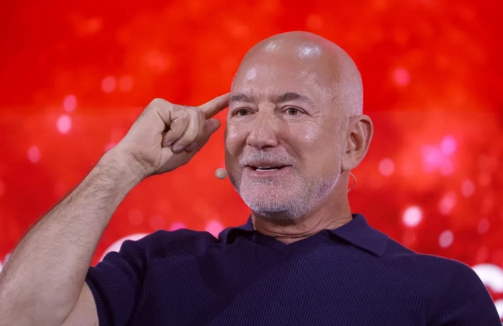 Jeff Bezos gesturing while speaking on stage against a red background
