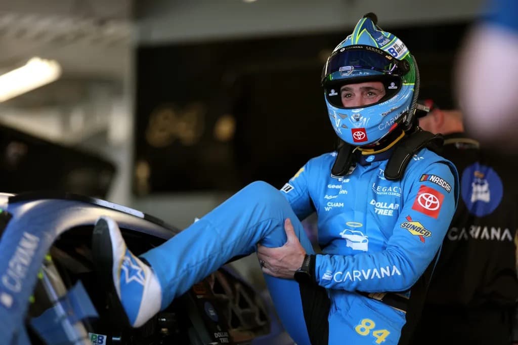 Jimmie Johnson in racing gear and helmet climbing into his NASCAR race car