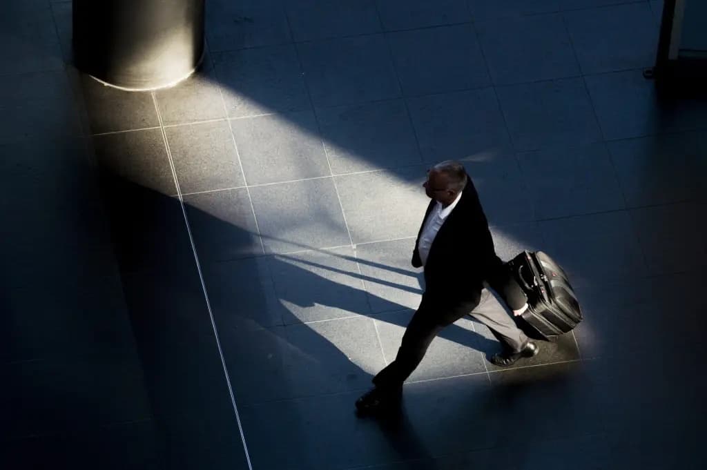 A businessman walking through an airport terminal with a rolling suitcase, lit by a shaft of light