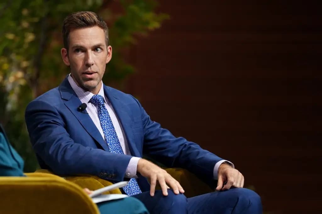 A man in a blue suit speaking while seated on a conference stage