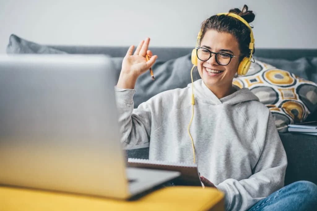 A remote worker smiling and waving during a video call from her living room