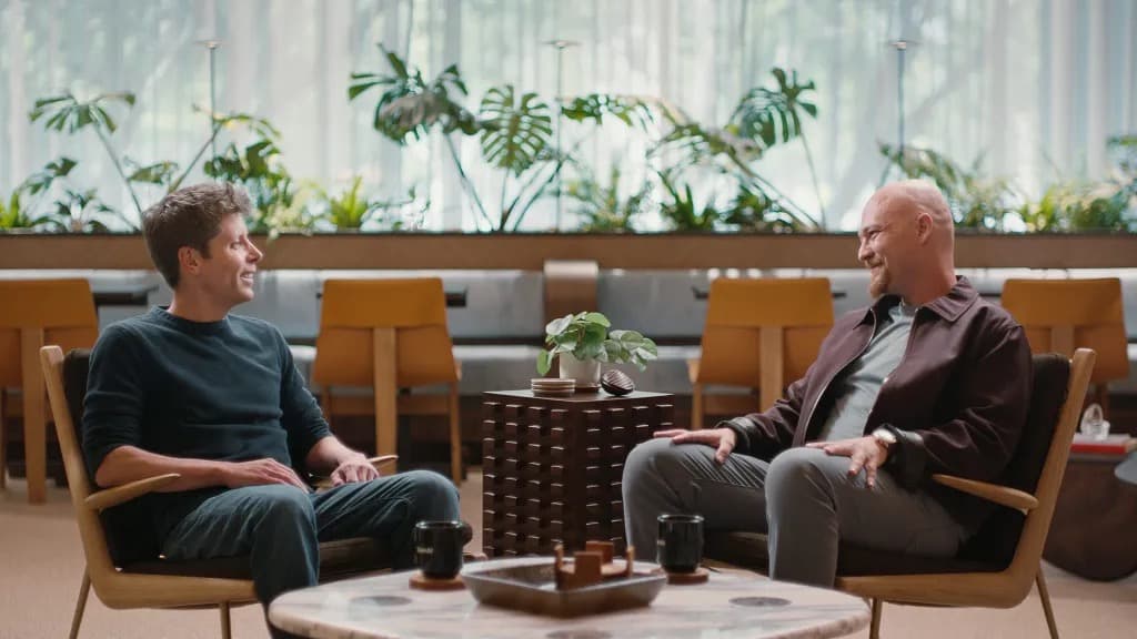 Two men sitting in armchairs having a conversation in a lounge with plants in the background