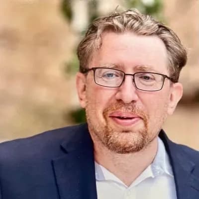 Portrait of Mark Minevich wearing glasses and a navy blazer