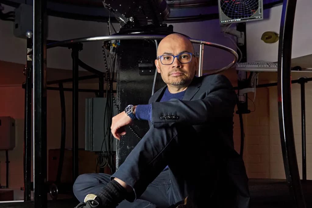 Demis Hassabis sitting on the floor of an observatory beneath telescope equipment
