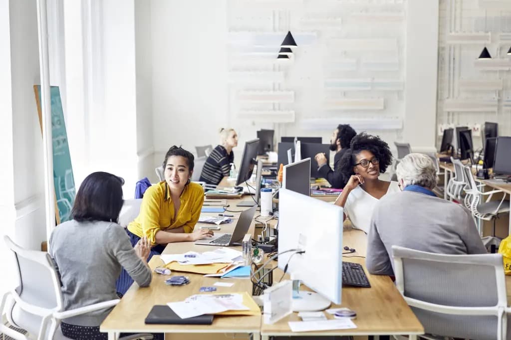 Colleagues talking and working together at desks in an open office
